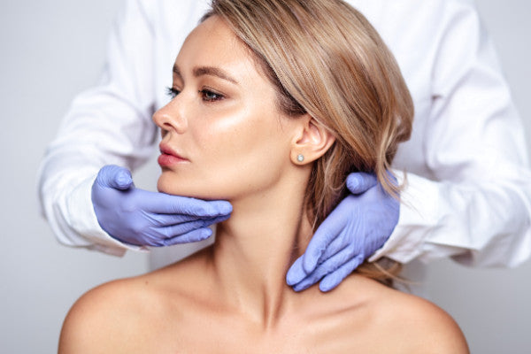 aesthetic doctor holds gloved hands beside face and neck of blonde haired woman