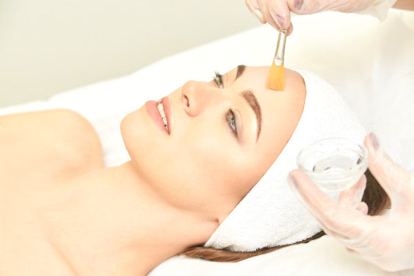 aesthetic doctor using brush chemical peel treatment to forehead of woman reclined on bed