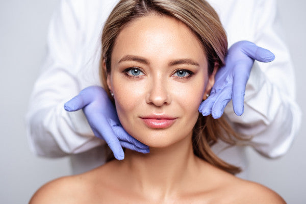 aesthetic doctor holds gloved hands beside face of blonde haired woman