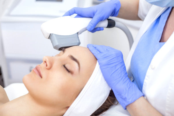 aesthetic doctor applying IPL treatment to forehead of brunette woman reclined on bed
