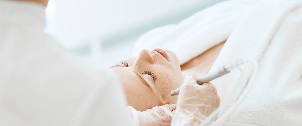 aesthetic doctor applying chemical peel solution to face of redhead woman reclined on bed